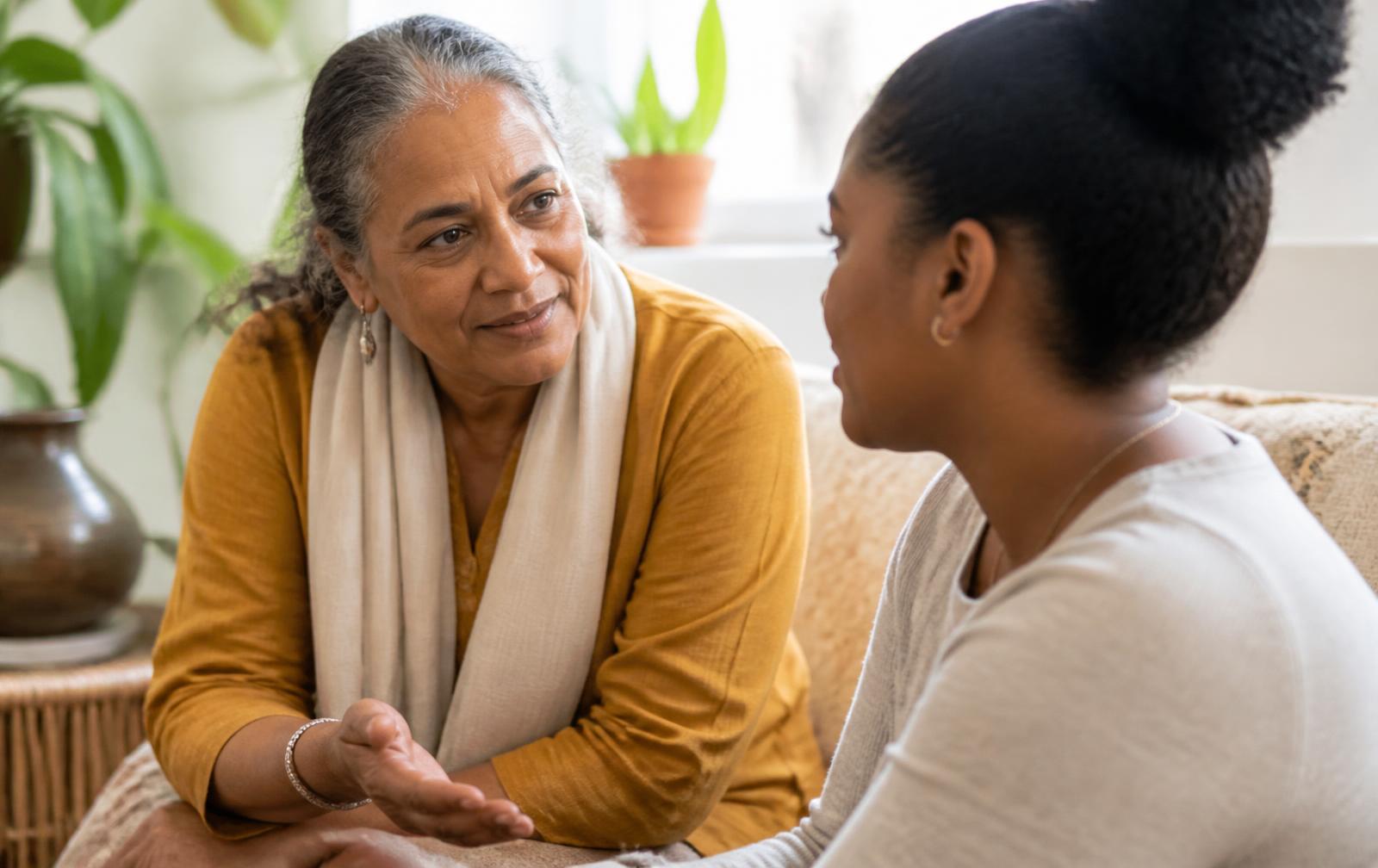 An older Indo-Caribbean woman mentor encouraging a young Afro-Caribbean woman in conversation